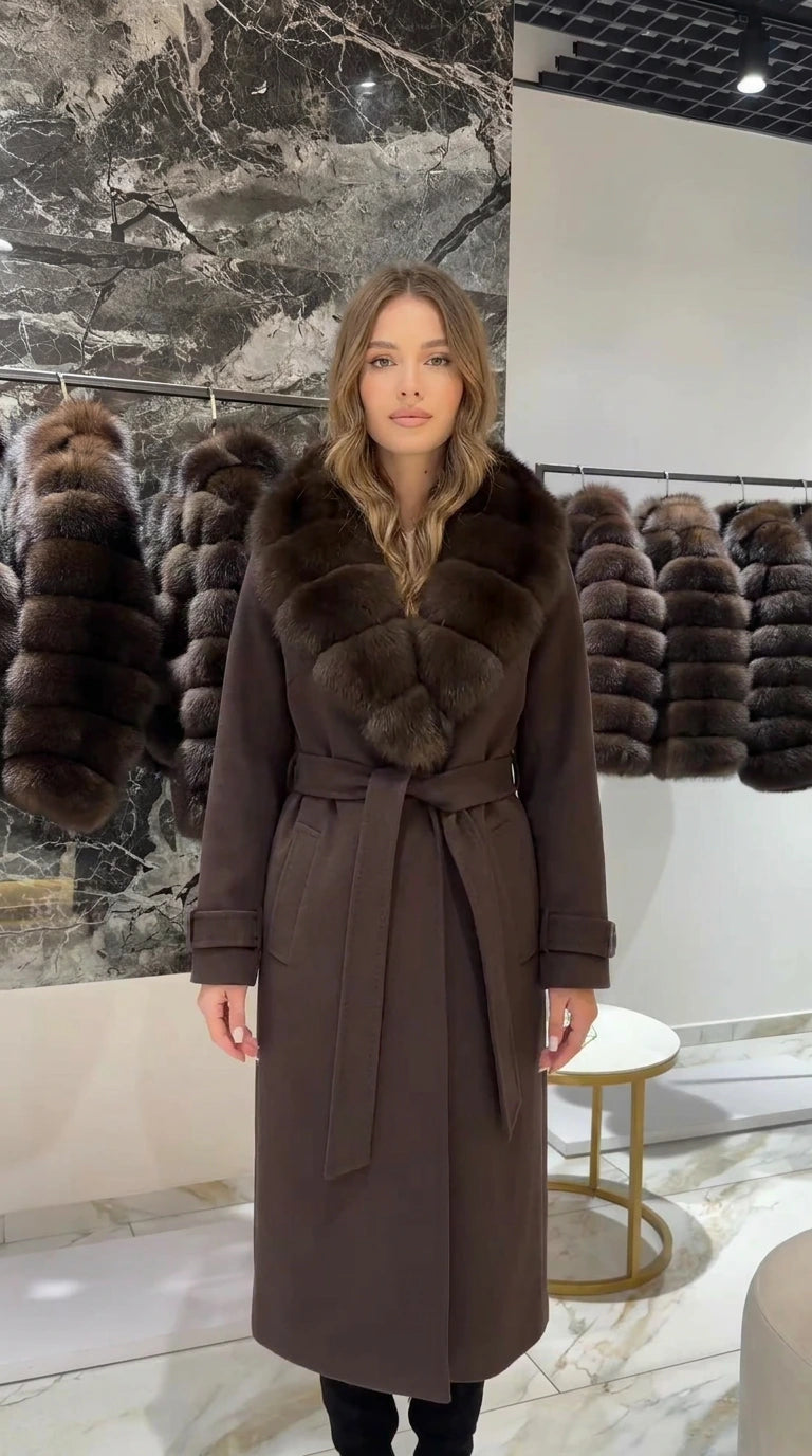 Front view of woman wearing a long chocolate brown belted coat with faux fur collar