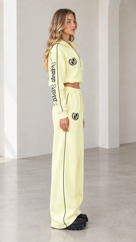 Side profile view of model in butter yellow tracksuit set showing sleeve embroidery and piping