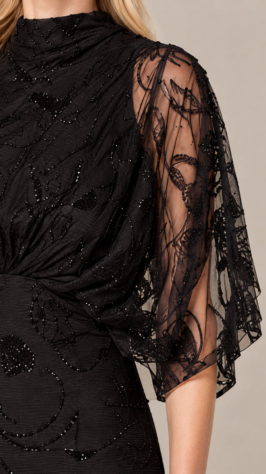 Close-up detail of sheer embroidered sleeve and beaded high neckline on black evening dress