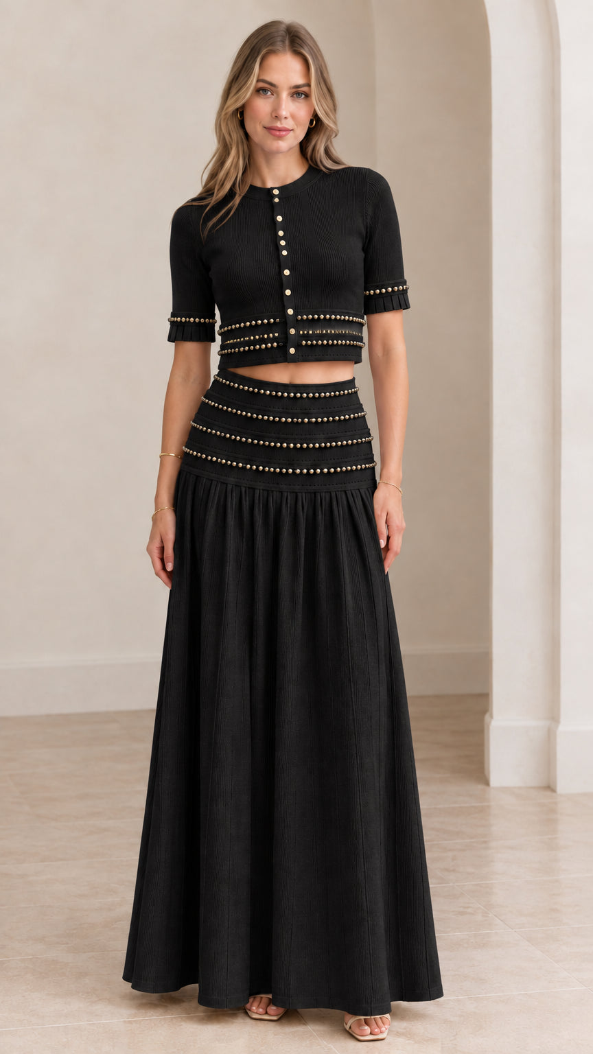 Model wearing black beaded crop top and matching drop-waist pleated maxi skirt