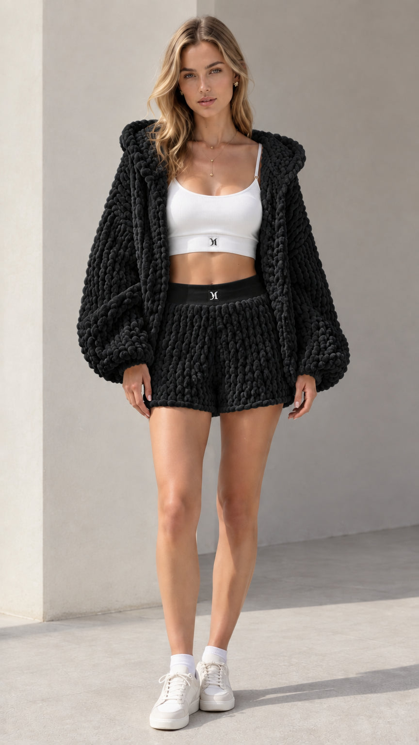 Model wearing black chunky knit hooded cardigan and high-waisted shorts set