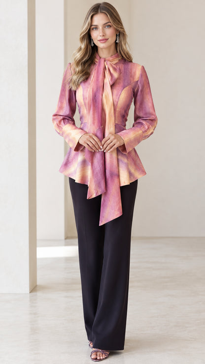 Model wearing Blush Pink long sleeve tie-neck peplum blouse paired with black wide-leg trousers, front full view