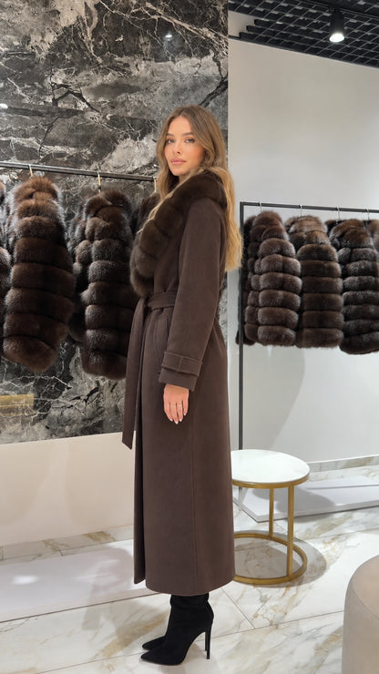 Side profile of woman wearing a long brown coat with waist tie and fur trim
