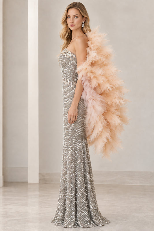Side profile of model in full-length silver beaded formal dress and dramatic feather cape