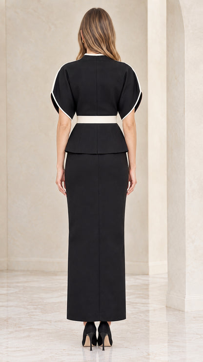 Back view of model wearing black peplum top and column maxi skirt set with white piping