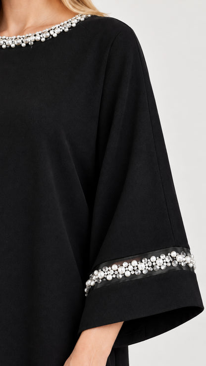 Close-up detail of faux pearl and bead trim on neckline and flared sleeve cuff