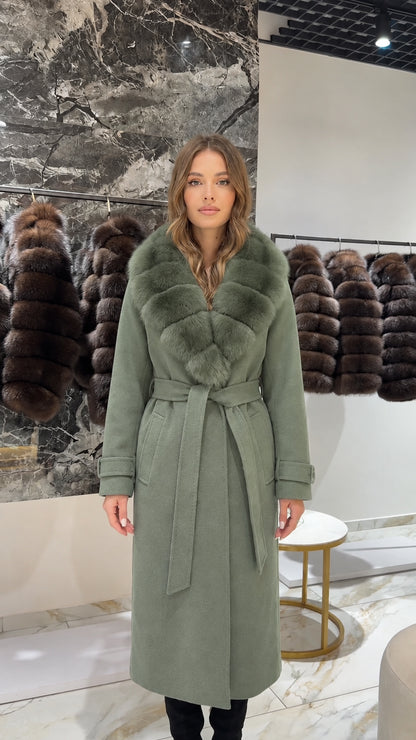 Front view of woman wearing a sage green long coat with tonal faux fur collar